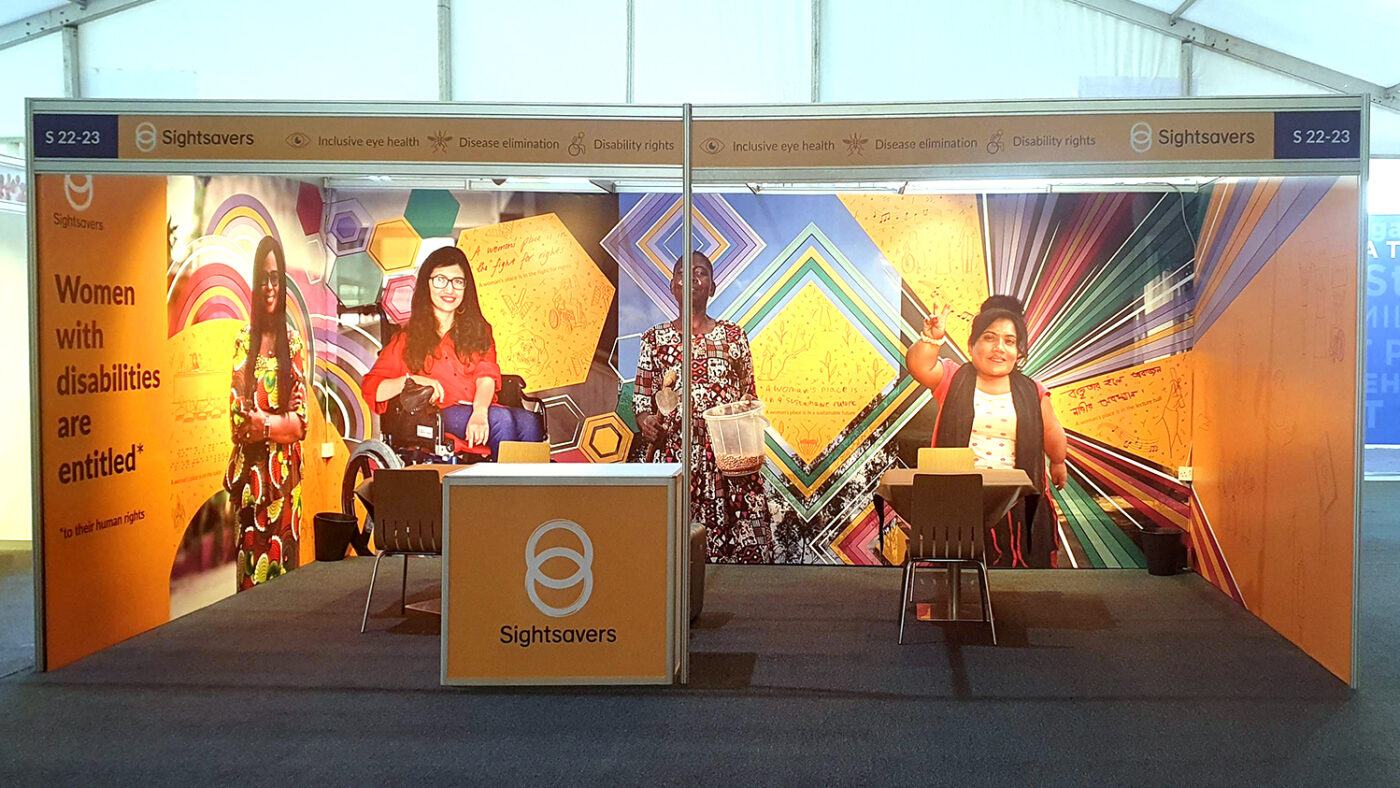 A colourful exhibition booth featuring illustrations and photos, plus the text 'Sightsavers' and 'Women are entitled - to their human rights'.