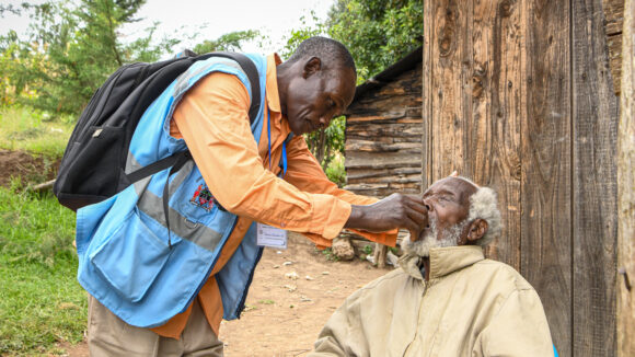 A health volunteer places medication in a villager's mouth in Kenya.