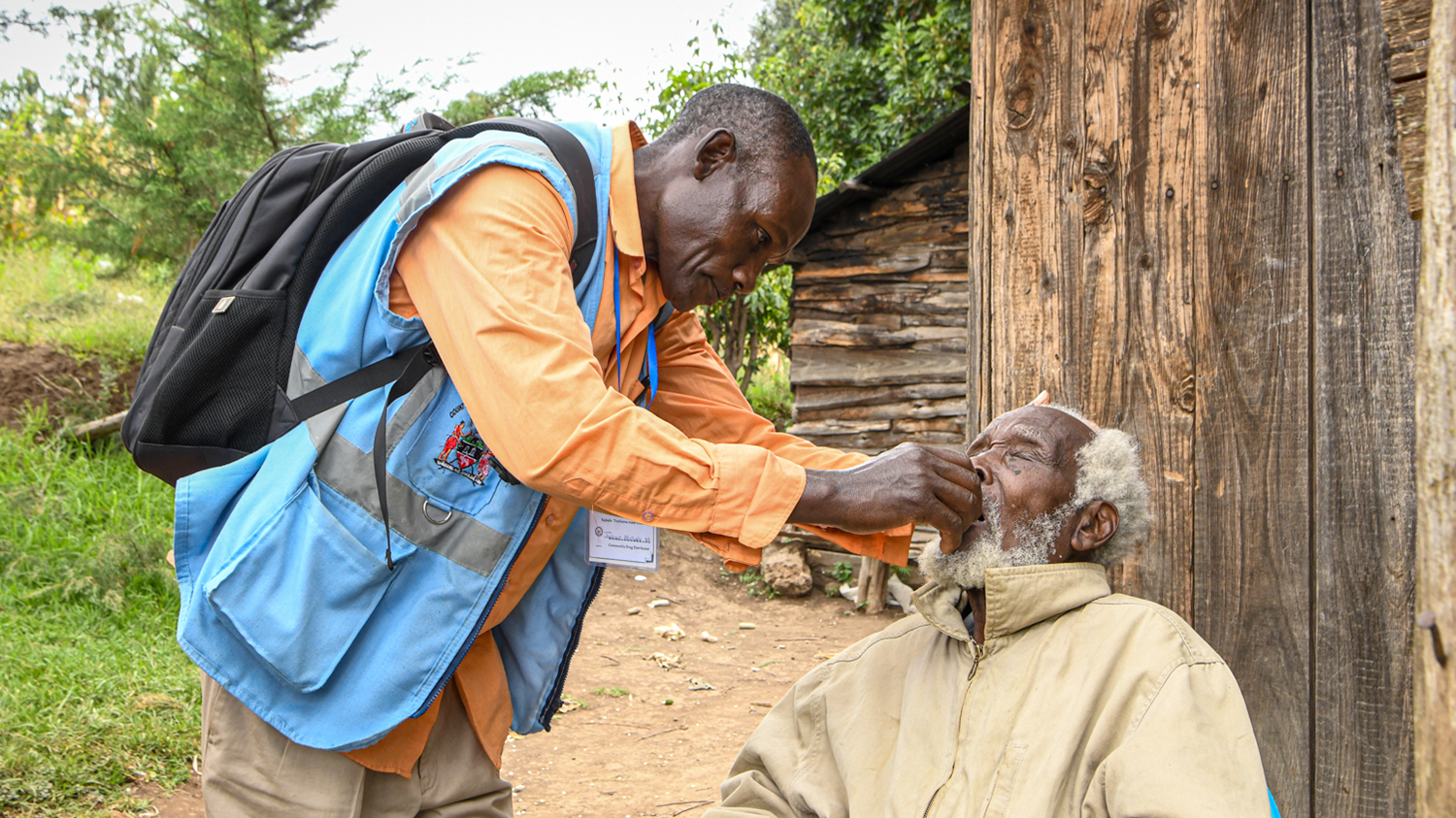 A health volunteer places medication in a villager's mouth in Kenya.