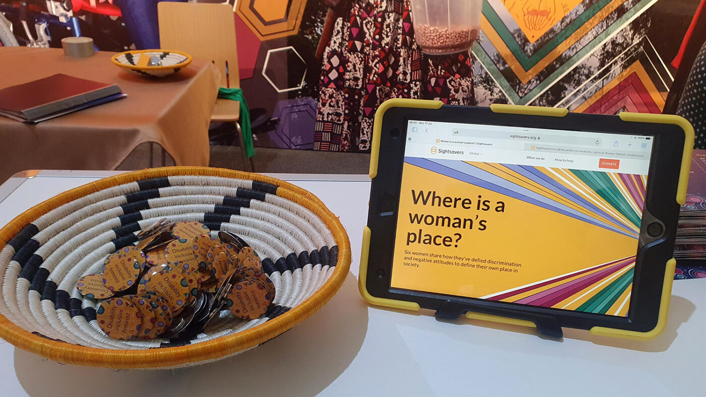 A close-up of Sightsavers stand at the conference, featuring a digital tablet and a bowl containing badges.