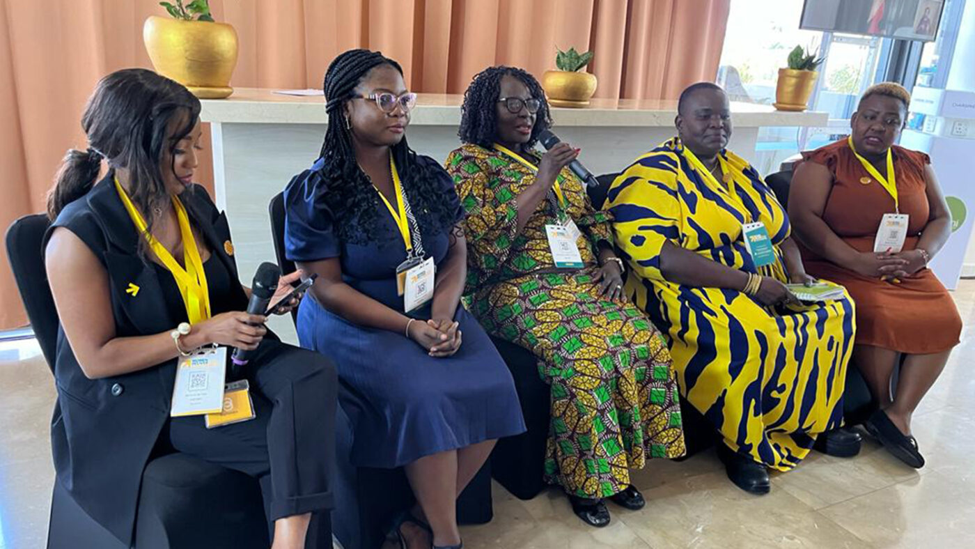 Five women sit in a row at the Women Deliver conference, one holding a microphone.