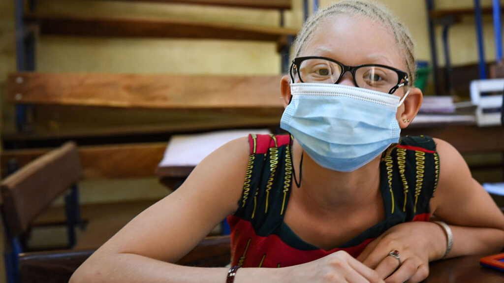 Wearing a surgical mask, Noutene reads braille at an inclusive school in Mali.
