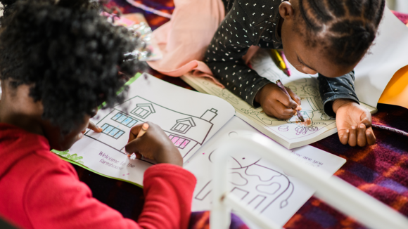 A young girl colours in a picture of a house.