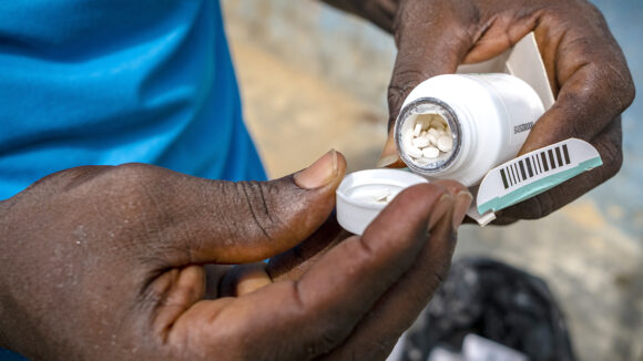 A health worker holds a pot of pills and pours some out into his hands.