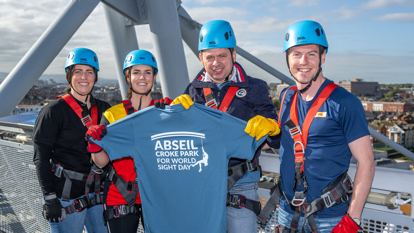 Four men and women from DHL pose wearing abseiling harnesses and protective headwear.