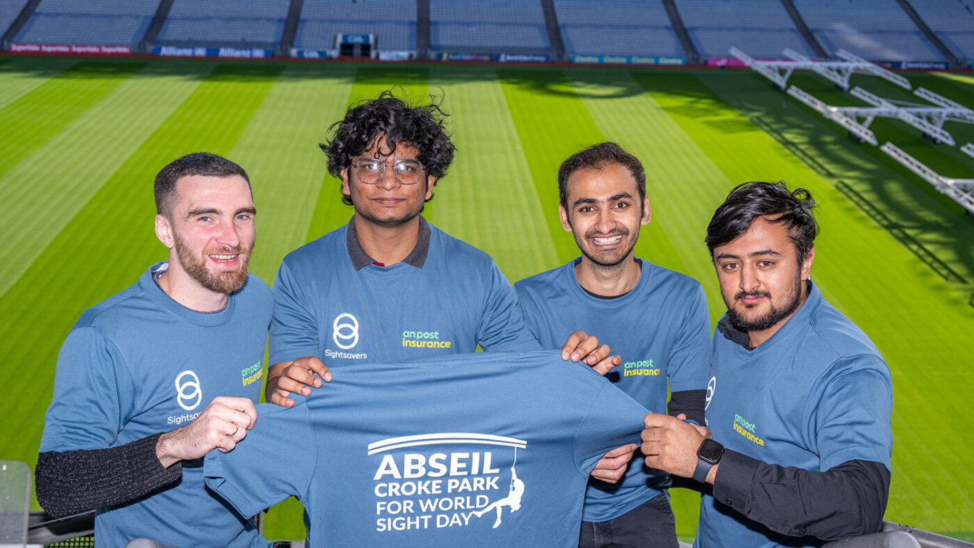 Four men from Michael Guineys hold up a t-shirt that reads 'Abseil Croke Park for World Sight Day'.