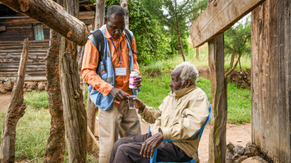 A community drug distributor hands an elderly man medication to treat trachoma.