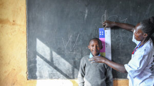 A female community drug distributor measures a girl to see how much medication she needs to protect her from trachoma.