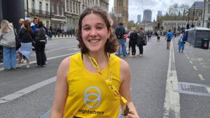 Charity runner Anya smiles broadly while holding her race medal.