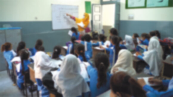 A blurred photograph of a school classroom in Pakistan.