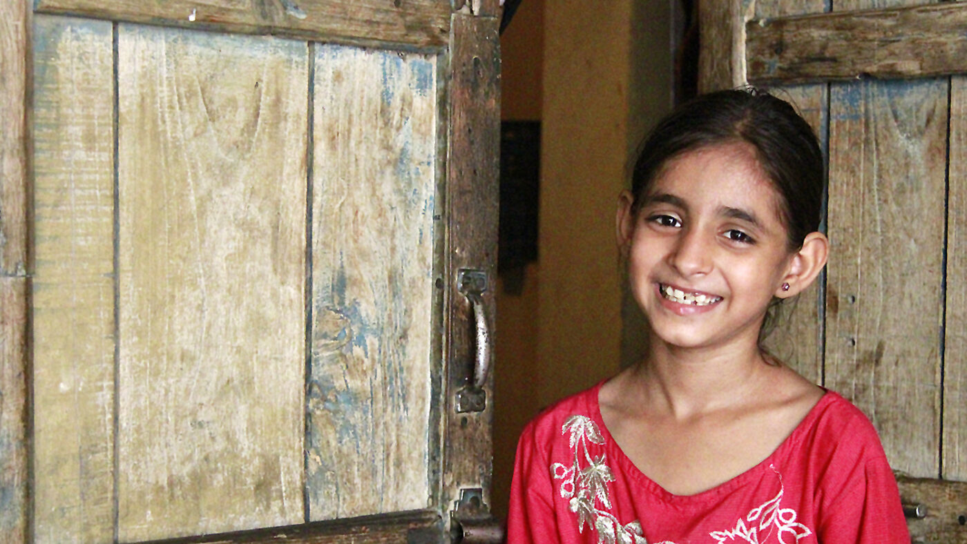 Nine-year-old Nayab smiles outside her home in Pakistan.
