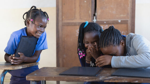 Three girls with disabilities sit around desks at an inclusive school in Zambia.