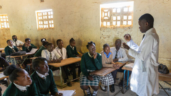 A teacher stands at the front of a classroom of teenage students.