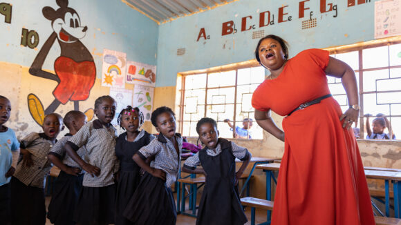 A female teacher leads children in a dance activity at school.
