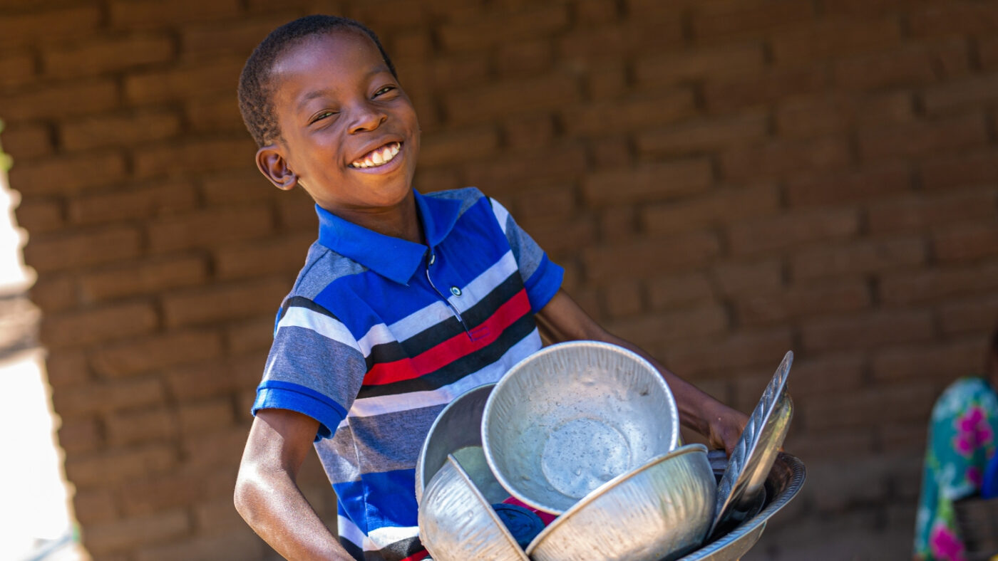 Mohamed smiles while carrying a pile of dishes.