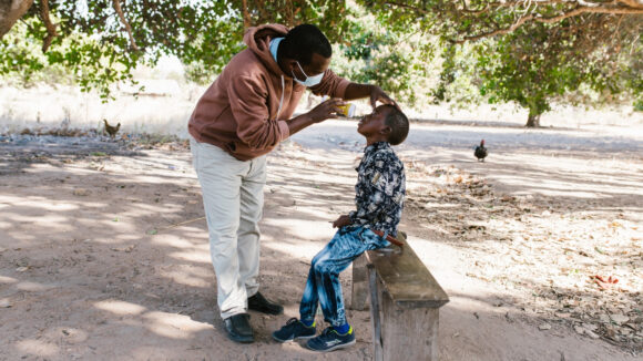 Mohamed sits down and looks up while his eyes are being examined.