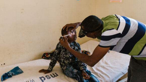 Mohamed sits on a hospital bed while his eyes are being examined