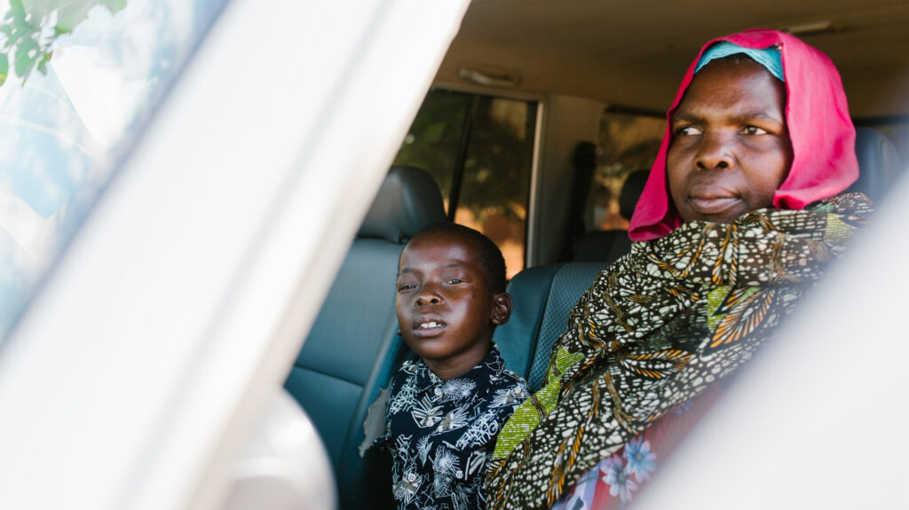 Mohamed sits in a car waiting to be taken to the hospital for his trichiasis operation. His grandmother, Sophia, is sat next to him.