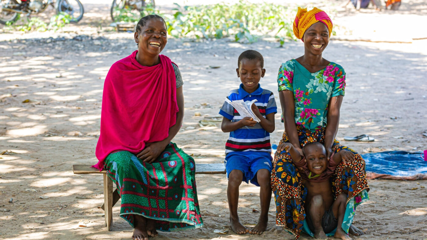 Mohamed sits outside with his family. They are all smiling and laughing together.