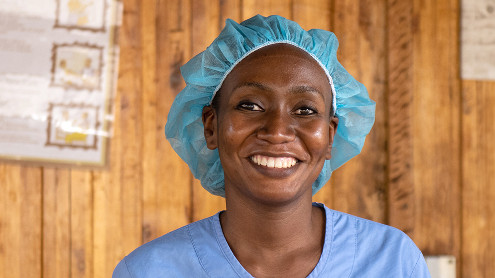 Dr Moira smiles at a clinic in Malawi. She's wearing blue surgical scrubs and a blue medical hair covering.
