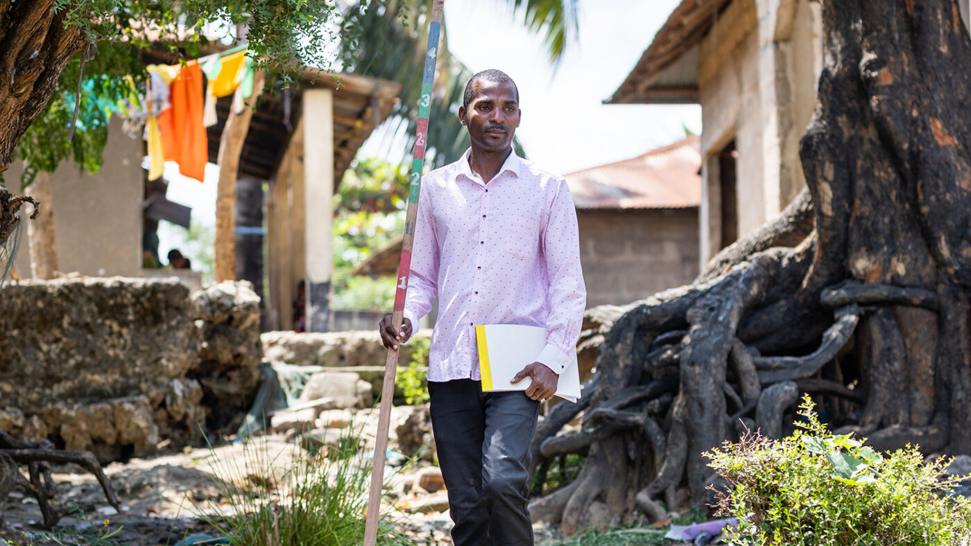 Seif walks through his village carrying a dose pole to measure people to determine how much medication they need.