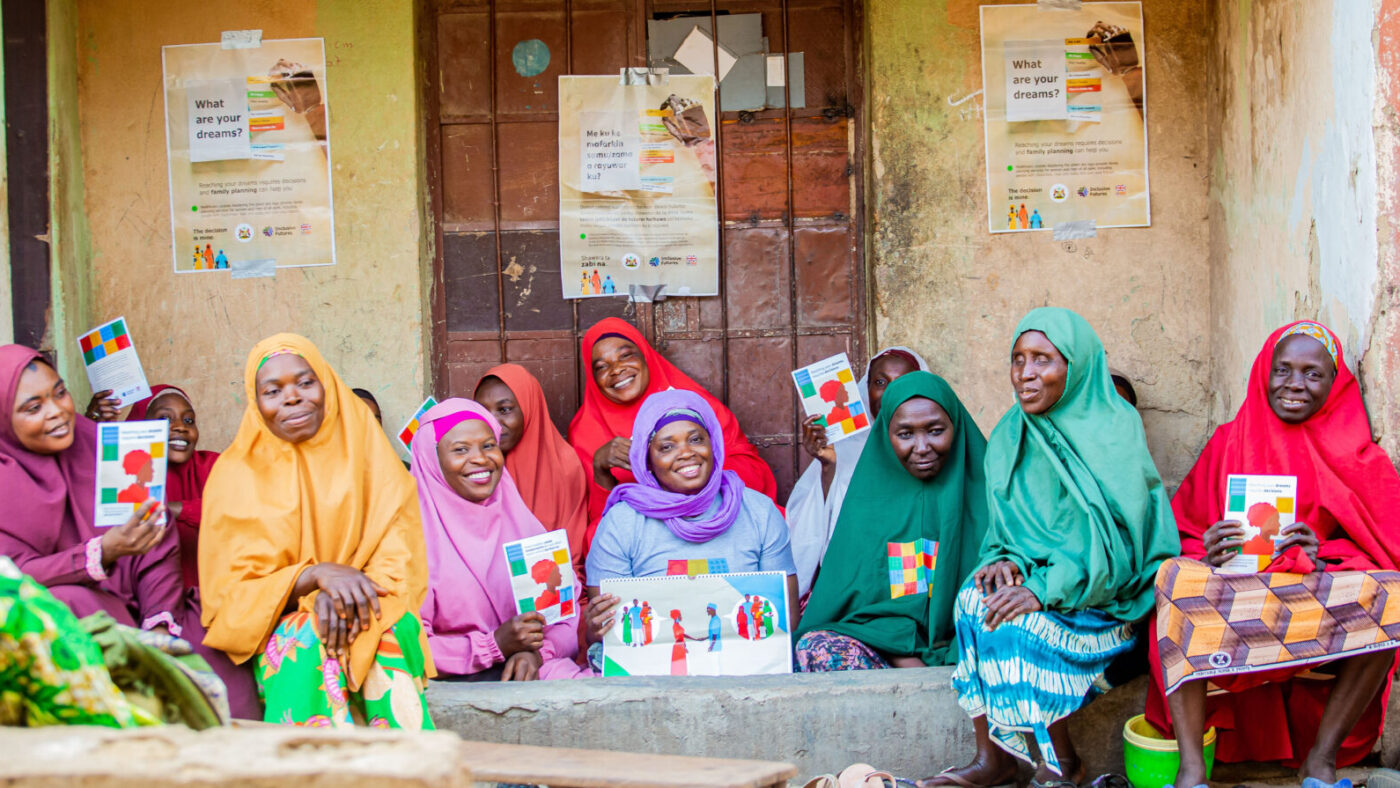 A group of smiling women in Nigeria hold posters and leaflets about family planning.