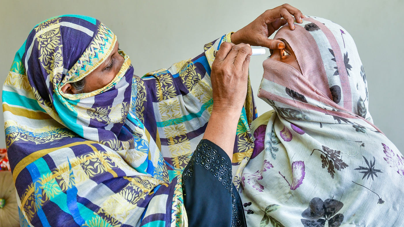 A woman examines a patient's eye with a torch.