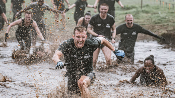 A smiling man runs through a river of mud during a Tough Mudder endurance event.