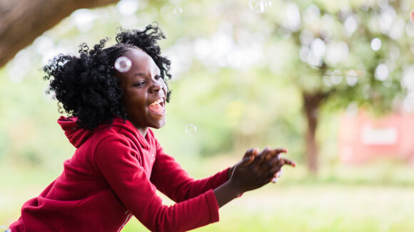 Seven-year-old Luyando smiling broadly and cheering as she plays with bubbles.