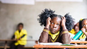 Luyando, a seven-year-old girl from Zambia, at school in her brown and yellow uniform. She is struggling to see and has eyes rolled her eyes back because of cataracts.