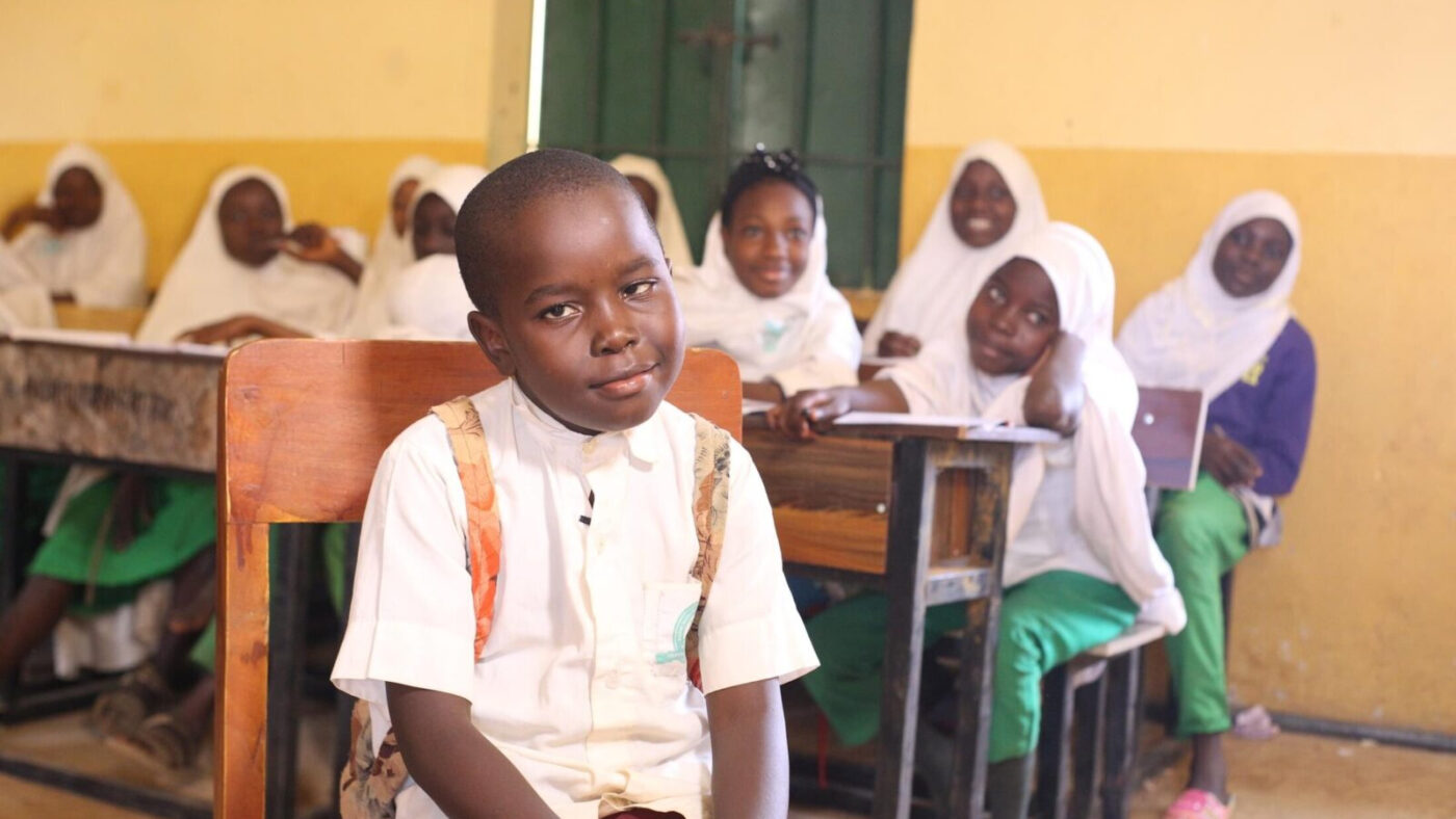 Abdul-Jabbar sits in a classroom and smiles. Other students sit behind him.
