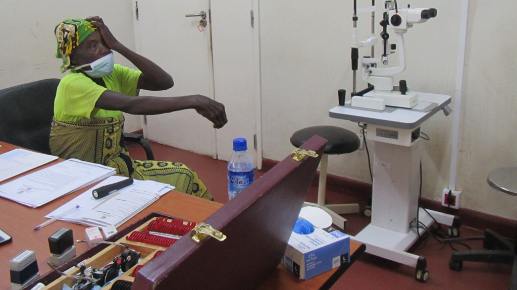 Caliha covers her left eye while sitting in a room full of eye examination equipment.