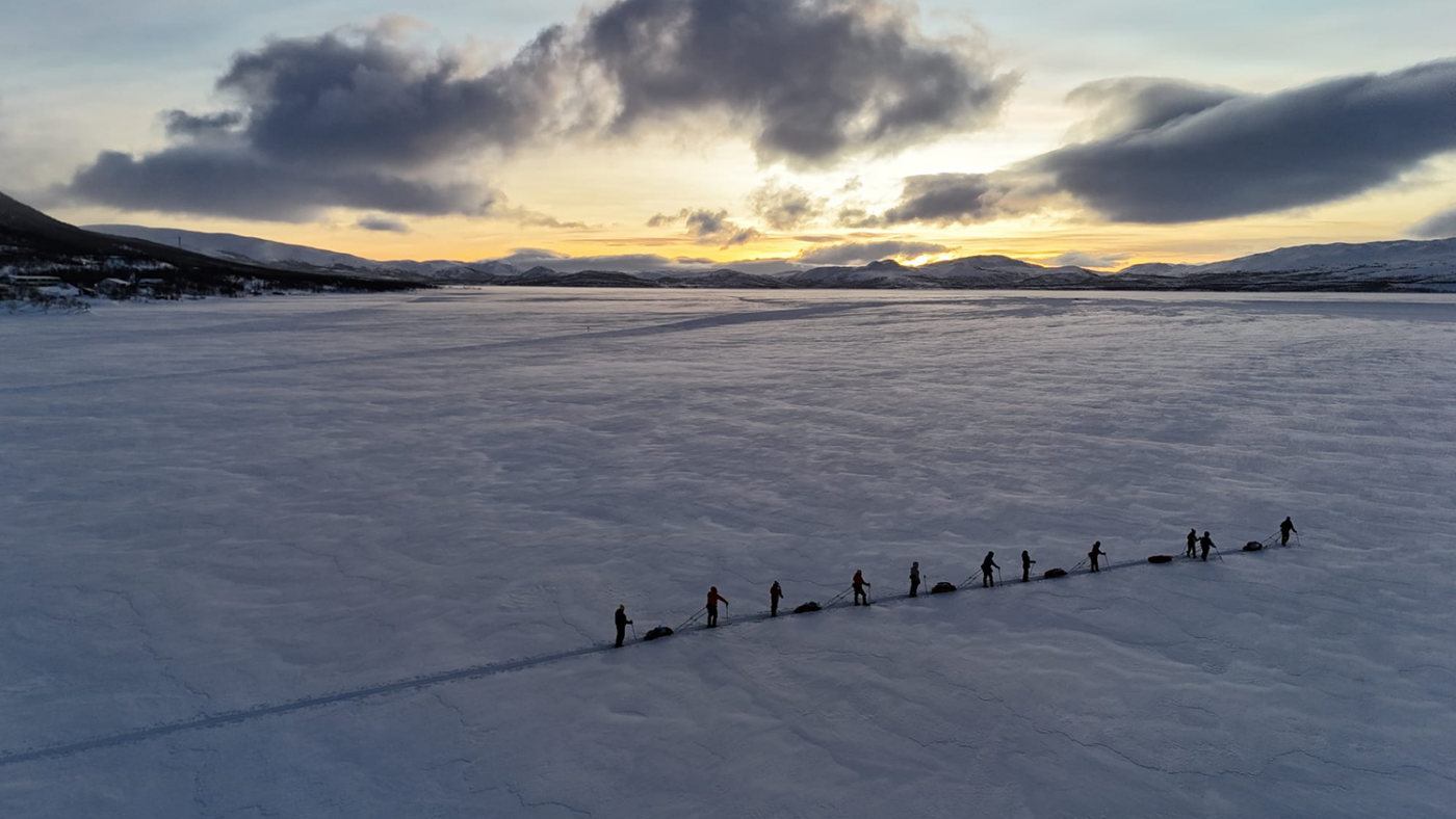 A small group of people trek across a frozen lake in the Arctic, pulling sledges behind them.