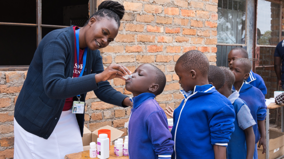 Melody provides children, lined up in blue school uniform, with medicine to protect them from trachoma at a school.