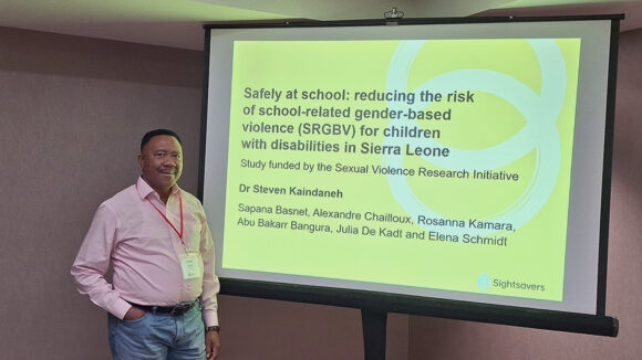 Steven Kaindaneh stands next to a screen during his presentation at the 2025 CIES conference.