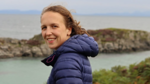 Sightsavers' employee Hannah smiles at the camera with the sea in the background.