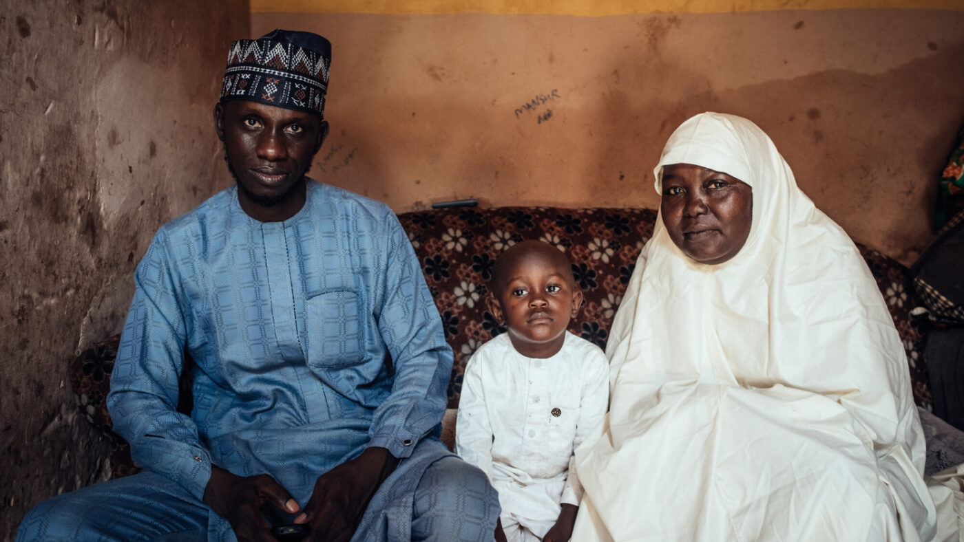 Muhammad sits inside his home, between his father, Abubakar, and grandmother, Halima.