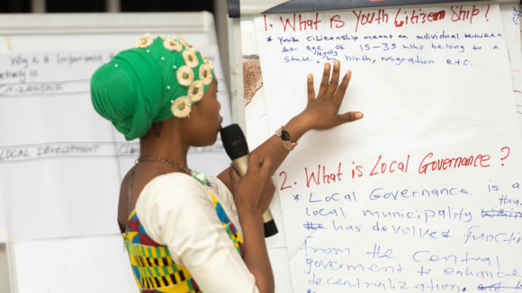 A woman holding a microphone points to a whiteboard that says 'what is youth citizenship?'.