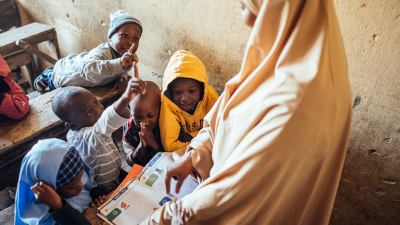 Muhammad and four other students sat at a table with their teacher pointing at textbooks in front of them.