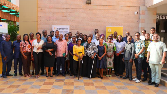 A large group of people gather for a photograph in front of a Sightsavers logo.