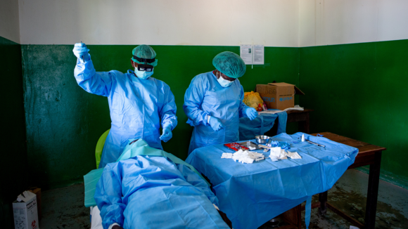 A basic operating room with a surgeon and nurse performing surgery on a patient. They all wear surgical overalls.