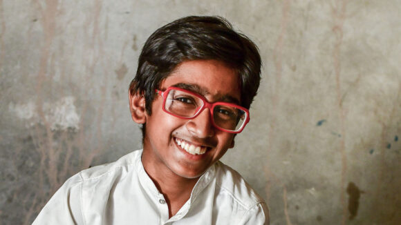 14-year-old Humair smiles while wearing a red pair of glasses.