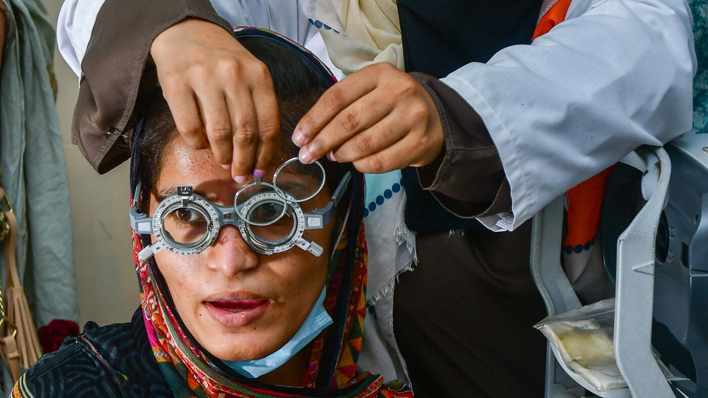 Aasiya wears a pair of optometry glasses while an eye technician changes the lenses.