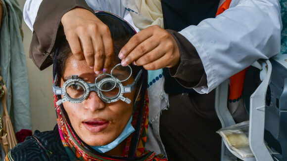 Aasiya wears a pair of optometry glasses while an eye technician changes the lenses.