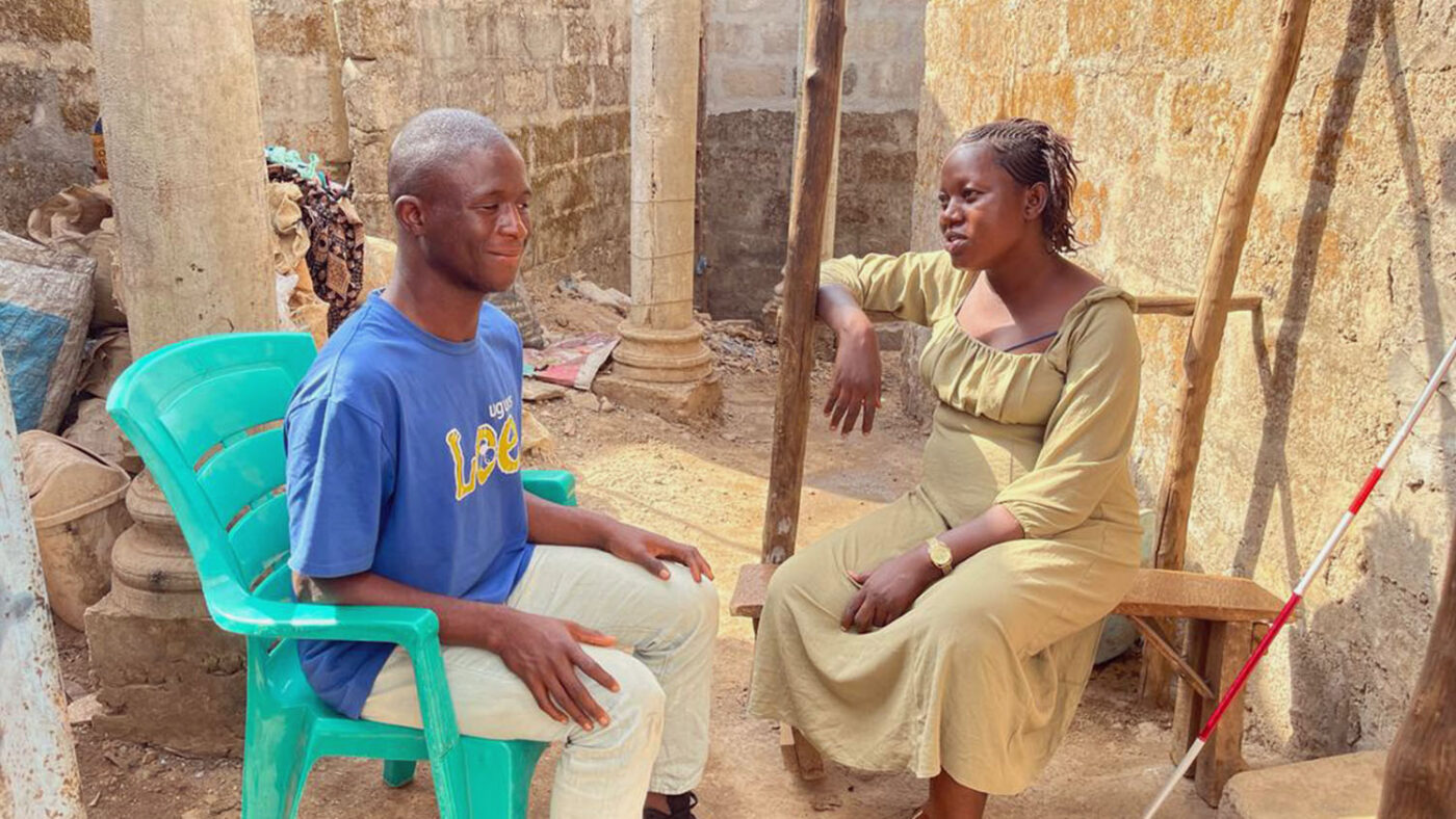 Abubakarr and Magdalene chat outside while sitting on plastic chairs.