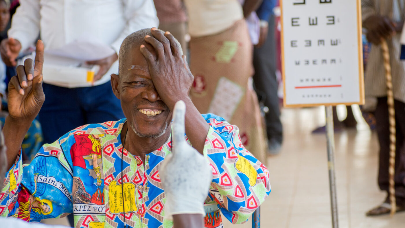 A man smiling covers one eye with his hand during an eye test.