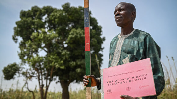 Community volunteer dispenser, John standing outside with his dose pole and sign.