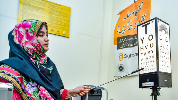 A female optometrist points to a row on a Snellen chart.