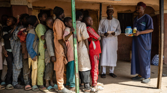 Pupils queue in front of a man who holds medication.