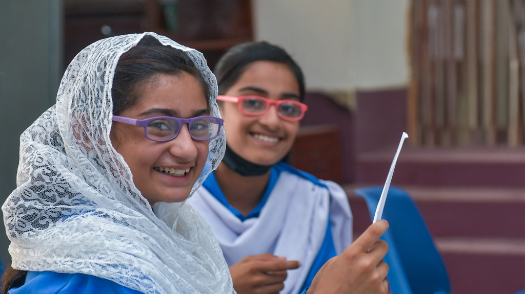 Two girls wearing glasses smile widely.
